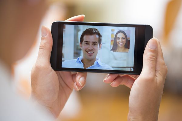 نمای نزدیک از یک دست زن که تلفن هوشمند را در حین تماس ویدیویی اسکایپ با دوستش در دست گرفته است