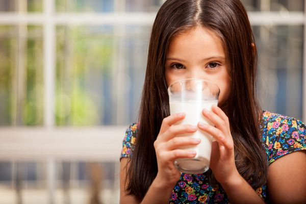 دختر بچه ای زیبا در حال نوشیدن یک لیوان شیر در خانه