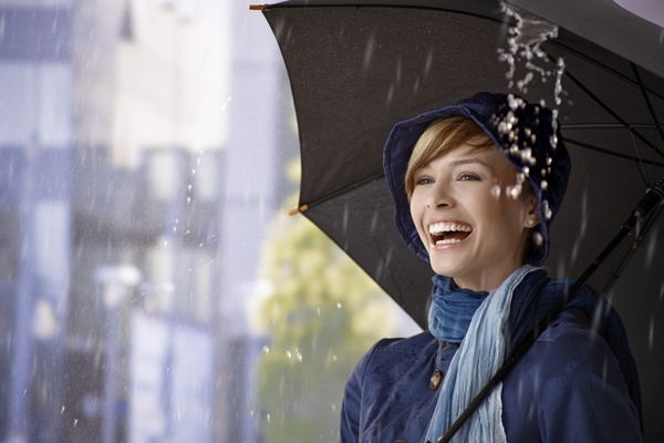 زن جوان شادی که زیر چتر زیر باران ایستاده و می خندد