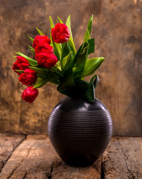 لاله های قرمز زیبا در گلدان مشکی روی زمینه چوبی