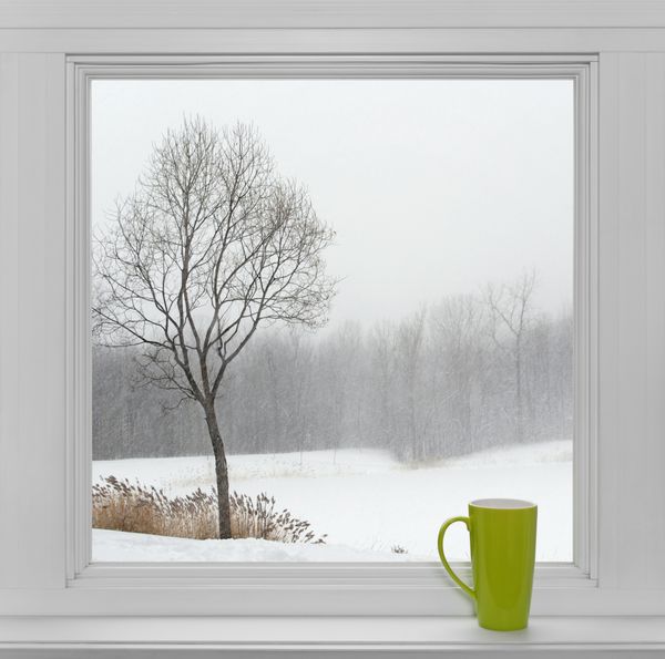 فنجان چای سبز روی طاقچه با چشم انداز زمستانی که از پنجره دیده می شود