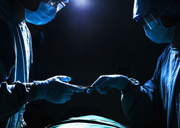 دو جراح که تجهیزات جراحی را در اتاق عمل کار می کنند و عبور می دهند