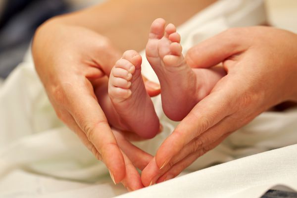 دست های مادر که قاب قلبی برای پاهای کوچک نوزاد تازه متولد شده اش را تشکیل می دهد