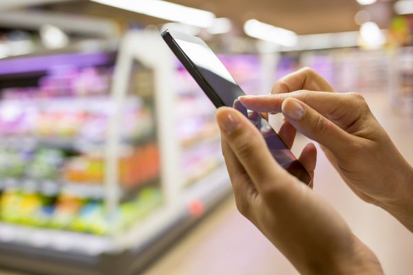 زن هنگام خرید در سوپرمارکت از تلفن همراه استفاده می کند
