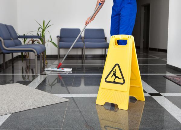 نمای نزدیک مرد در حال تمیز کردن زمین با علامت زرد رنگ کف مرطوب