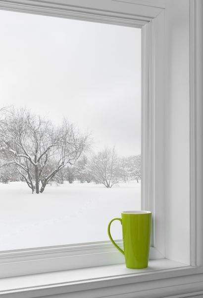 فنجان سبز روی طاقچه با چشم انداز زمستانی که از پنجره دیده می شود