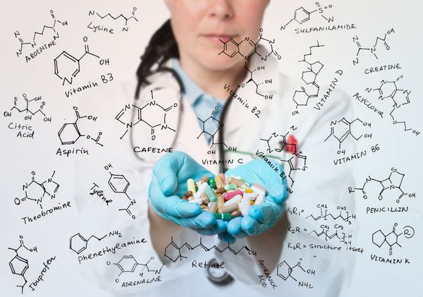 کارمند بهداشت و درمان با دستان پر از قرص احاطه شده با فرمول آنتی بیوتیک ویتامین ها و افزودنی های غذایی