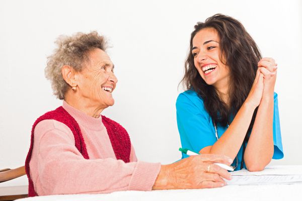 بانوی مسن شاد در حال خنده با پرستار مهربانی که در خانه مراقبت می کند