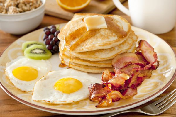 نمای نزدیک از یک بشقاب صبحانه با پنکیک تخم مرغ بیکن و میوه