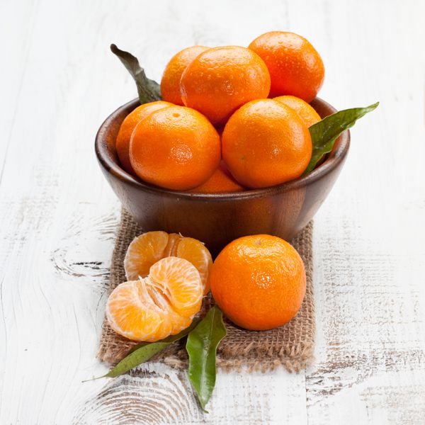 نارنگی های رسیده خوش طعم با برگ های روی میز چوبی سفید