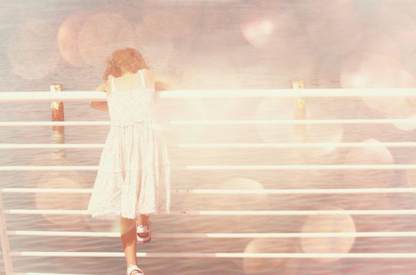 کودک خردسالی که نزدیک حصار کنار دریا ایستاده است افکت رویایی نور بوکه