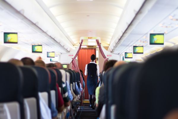 فضای داخلی هواپیما با مسافران روی صندلی و مهماندار که در راهرو راه می روند