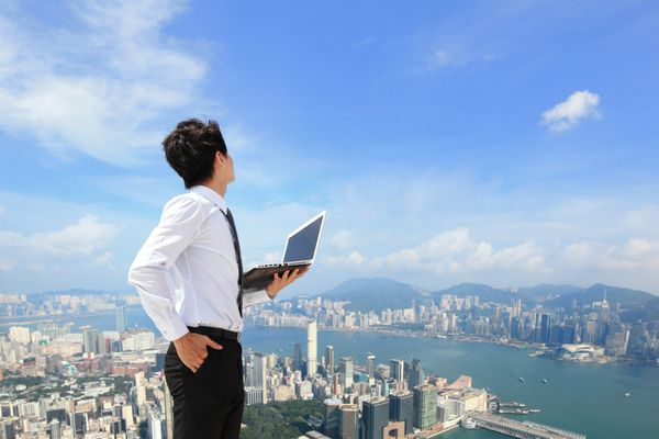 مرد جوان تجاری با استفاده از لپ تاپ و نگاه به منظره شهری آسیایی هنگ کنگ