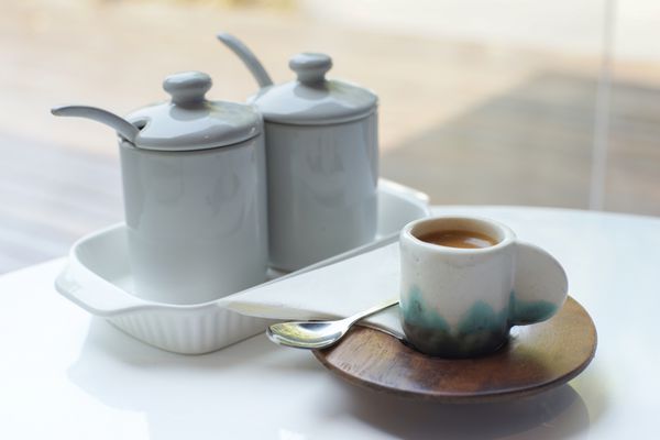 فنجان کوچک قهوه روی میز سفید با مجموعه ای از گلدان های شکر