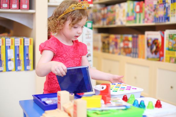 دختر کوچک زیبا در تاج شاهزاده خانم با اسباب بازی های موجود در فروشگاه بازی می کند