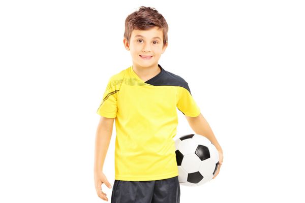 بچه ای با لباس ورزشی که یک توپ فوتبال جدا شده روی پس زمینه سفید در دست دارد