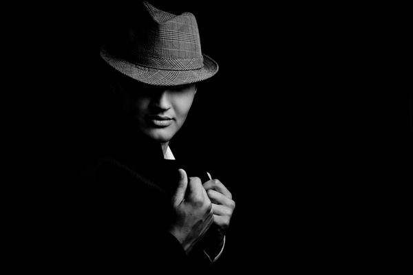 پرتره کم کلید از گانگستر جوان با کلاه در تاریکی تصویر سیاه و سفید
