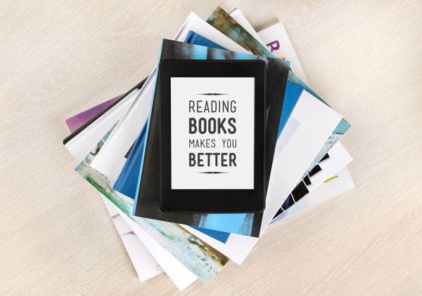 خواندن کتاب شما را بهتر می کند - متن روی صفحه کتاب الکترونیکی در بالای انبوهی از کتاب ها و مجلات مفهوم یادگیری دانش جدید خودسازی و رشد توانایی های ذهنی