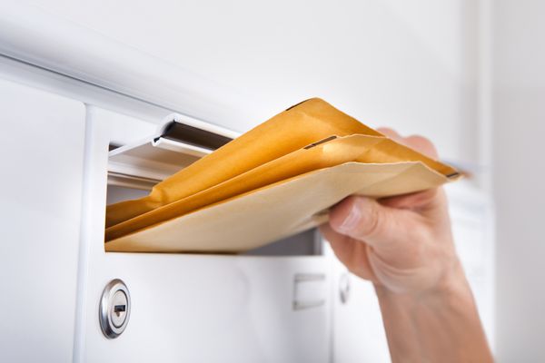 نمای نزدیک از پستچی که نامه ها را در صندوق پست می گذارد