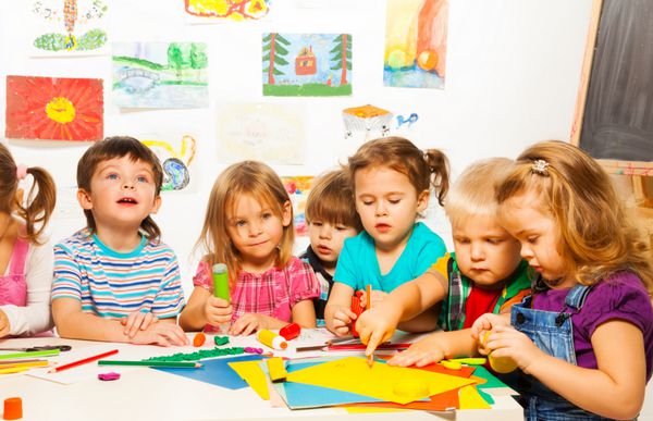 گروهی از بچه های کوچک نقاشی با مداد و چسباندن با چسب در کلاس هنر در مهد کودک