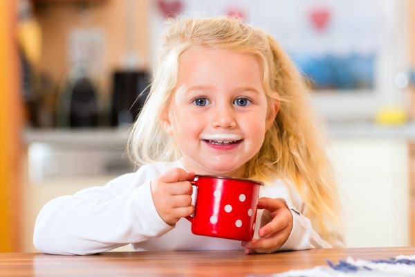 کودک در حال نوشیدن فنجان یا لیوان شیر در آشپزخانه خانگی