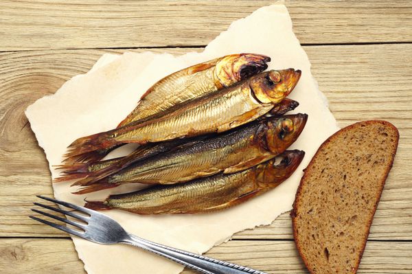 ماهی دودی طلایی روی کشتی با چنگال و نان