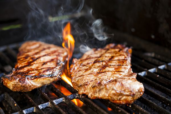 استیک های گوشت گاو در حال پختن در شعله باز روی بیکیو گریل