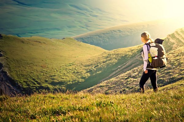 مسافر زن با کوله پشتی پیاده روی در کوه ها با منظره تابستانی زیبا در زمینه مفهوم سبک زندگی ورزشی کوهنوردی