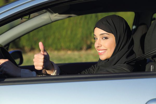 زن خوشبخت عربستانی عرب در حال رانندگی با یک ماشین با شست بالا و با روسری لبخند می زند
