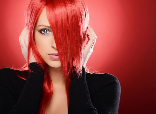 زن مو قرمز زیبا که روی پس زمینه قرمز ژست گرفته است