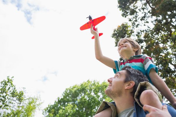 نمای پایین پسری با هواپیمای اسباب بازی که روی شانه های پدر در پارک نشسته است
