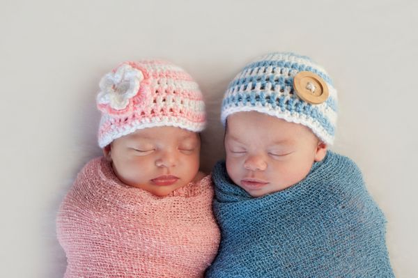 نوزادان تازه متولد شده دوقلوی برادر و پسر پنج هفته ای خوابیده کلاه های راه راه صورتی و آبی قلاب بافی بر سر دارند