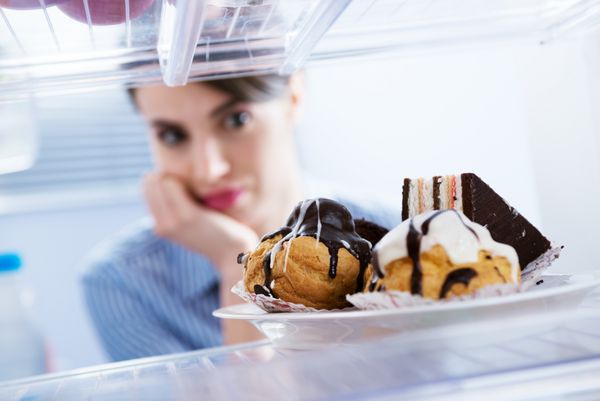زن جوان گرسنه جلوی یخچال هوس شیرینی شکلاتی می کند