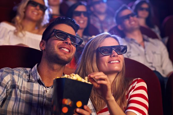 زوج شادی که در سینما نشسته اند در حال تماشای فیلم سه بعدی هستند در حال خوردن ذرت بو داده لبخند می زنند