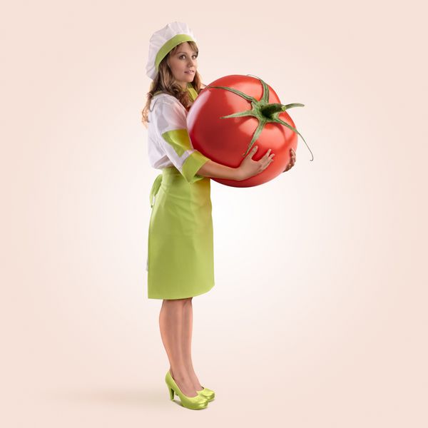 دختر آشپزی که یک گوجه‌فرنگی بزرگ روی پس‌زمینه بژ در دست دارد