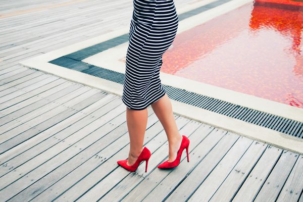 لباس زنانه شیک رترو با لباس راه راه مشکی و سفید پاشنه بلند قرمز کلاسیک ژست در نزدیکی استخر قرمز خلاقانه