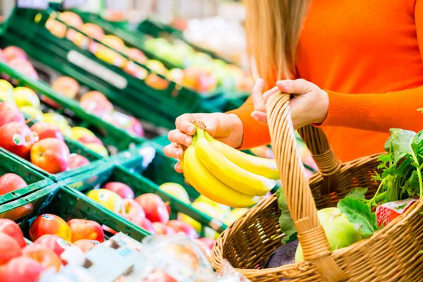 زن در سوپرمارکت در قفسه میوه برای خرید مواد غذایی او یک موز را در سبد خود می گذارد