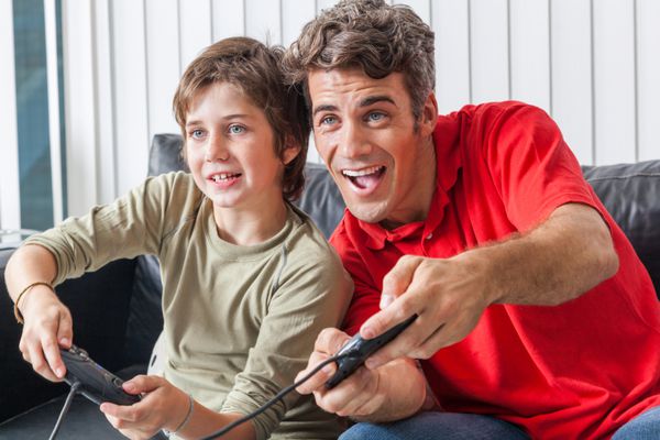 بازی ویدیویی پدر و پسر شاد در خانه کنترلر کنسول با لبخند هیجان زده در دست نشسته روی مبل