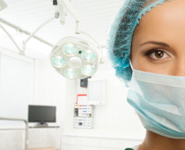زن جوان دکتر با کلاه و ماسک f در فضای داخلی اتاق جراحی