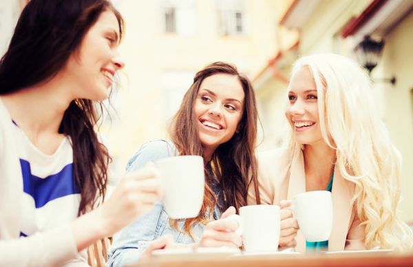 مفهوم تعطیلات و گردشگری - دختران زیبا در حال نوشیدن قهوه در کافه