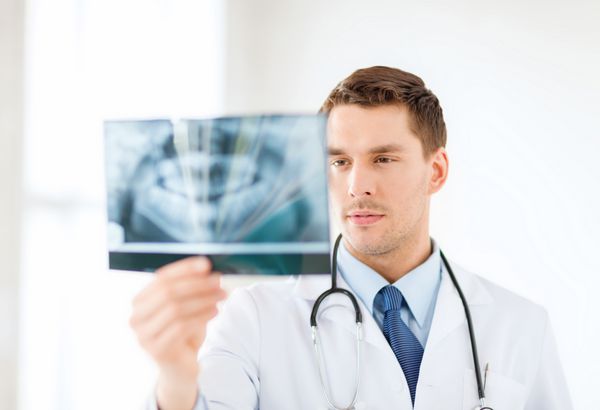 مفهوم پزشکی و مراقبت های بهداشتی - پزشک یا دندانپزشک مرد نگران که در بیمارستان به اشعه ایکس نگاه می کند