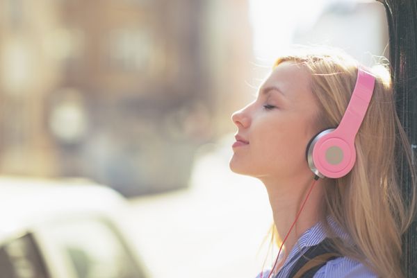 زن جوان در حال گوش دادن موسیقی با هدفون در شهر