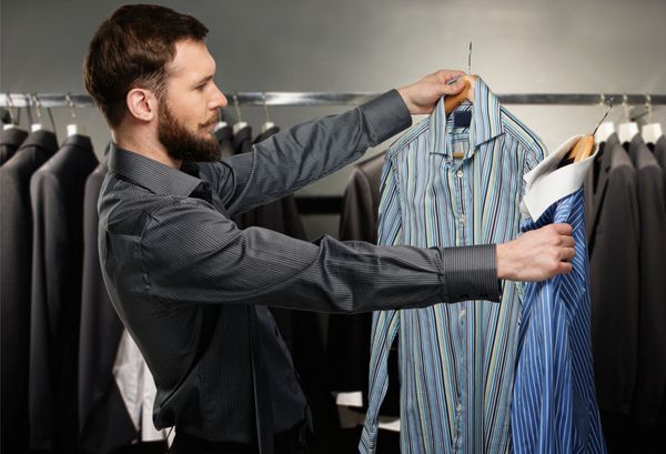 مرد خوش تیپ با ریش در یک مغازه پیراهن انتخاب می کند