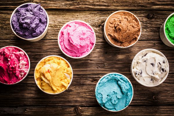 مجموعه ای از طعم های لذیذ بستنی ایتالیایی در رنگ های زنده که در وان های پلاستیکی جداگانه روی میز چوبی روستایی قدیمی در یک بستنی فروشی نمای بالای سر سرو می شود