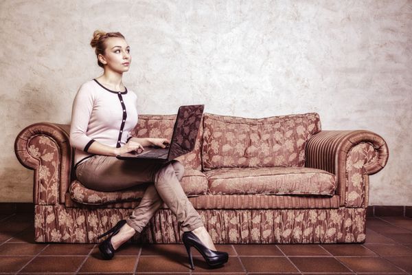 فناوری اینترنت مفهوم سبک زندگی مدرن زن تاجر متفکر یا دختر دانشجو با استفاده از لپ‌تاپ که روی رایانه کار می‌کند و روی کاناپه رترو نشسته است داخلی وینتیج po