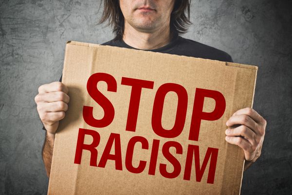 مردی که بنر مقوایی با پیام توقف نژادپرستی در دست دارد
