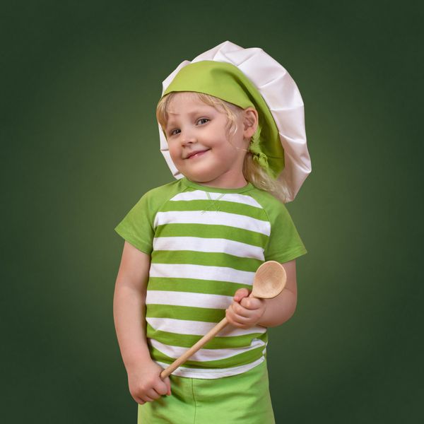 کودک سرآشپز خندان با یک قاشق چوبی بزرگ در زمینه سبز