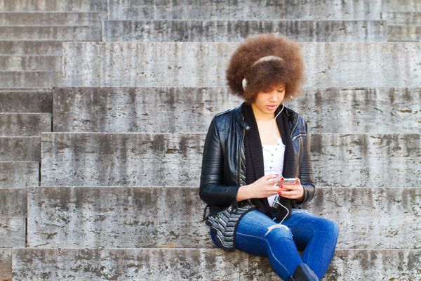 دختری با تلفن هوشمند روی راه پله نشسته است