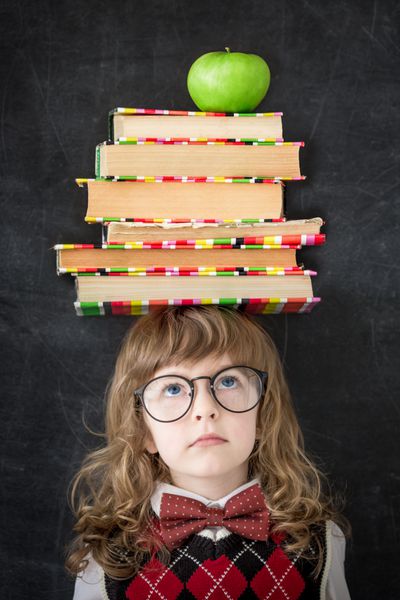 بچه باهوش در کتابخانه دانش آموز با کتاب های درسی و سیب سبز در برابر تخته سیاه مفهوم آموزش و پرورش