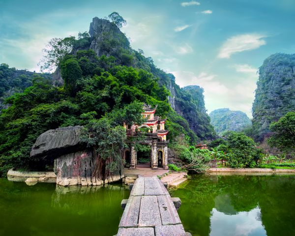 منظره پارک در فضای باز با دریاچه و پل سنگی ورودی دروازه مجتمع بتکده باستانی بیچ دونگ نین بین مقصد سفر ویتنام